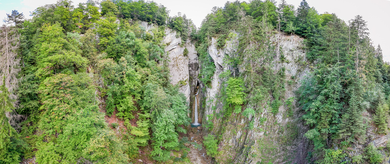 Aerial view of Grandvillard Waterfall cascading down steep rocky cliffs surrounded by a lush green forest in Grandvillard Fribourg Switzerland.