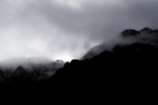 View of dark mountain silhouettes partially hidden by thick white mist and low clouds under a moody sky Hallstatt Upper Austria Austria. View of dark mountain silhouettes partially hidden by thick white mist and low clouds under a moody sky Hallstatt Upper Austria Austria.