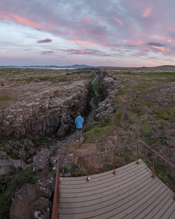Aerial view of Thingvellir National Park with a person on a wooden platform overlooking the rugged volcanic gorge under a pink sunset sky in Selfoss Blaskogabyggd Iceland. Aerial view of Thingvellir National Park with a person on a wooden platform overlooking the rugged volcanic gorge under a pink sunset sky in Selfoss Blaskogabyggd Iceland.