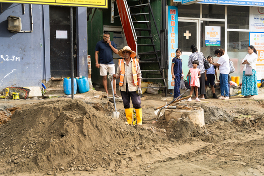 Sri Lanka 20 February 2026 View of a construction worker in a high visibility vest and straw hat standing by a pile of dirt on a busy urban street.