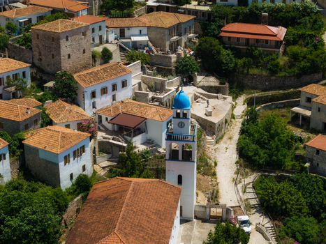 Aerial view of the historic village featuring traditional stone houses with terracotta roofs and a white church tower with a blue dome Dhermi Vlore County Albania. Aerial view of the historic village featuring traditional stone houses with terracotta roofs and a white church tower with a blue dome Dhermi Vlore County Albania.