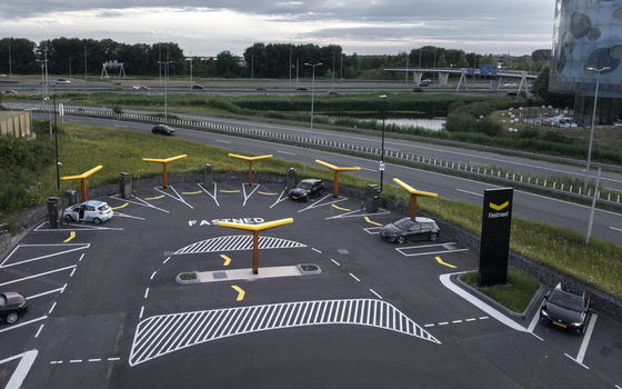 Aerial view of a Fastned electric vehicle charging station with yellow solar canopies and parked cars located near a highway in Amsterdam Noord Holland Netherlands. Aerial view of a Fastned electric vehicle charging station with yellow solar canopies and parked cars located near a highway in Amsterdam Noord Holland Netherlands.