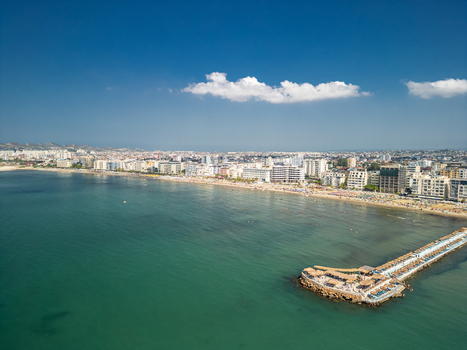 Aerial view of Hawaii Beach with its long pier extending into the turquoise Adriatic Sea lined with sandy shores and the urban skyline of Durres Durres Albania.