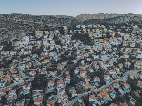 Aerial view of residential houses with swimming pools nestled on a hillside with winding roads and a rocky mountain backdrop in Calp Valencian Community Spain. Aerial view of residential houses with swimming pools nestled on a hillside with winding roads and a rocky mountain backdrop in Calp Valencian Community Spain.