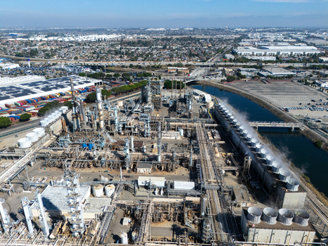 Aerial view of an oil refinery featuring complex industrial infrastructure cooling towers and storage tanks situated near a canal in the urban landscape of Carson California United States.