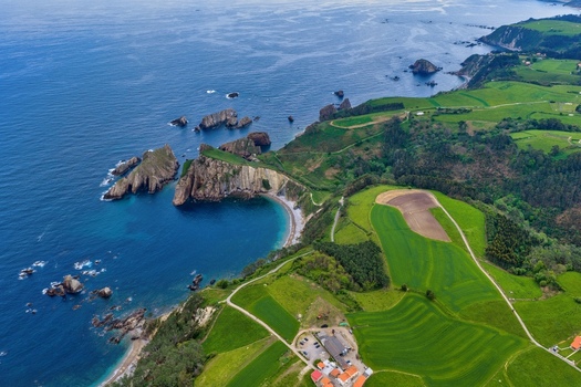 Aerial view of Silence Beach Viewpoint with dramatic cliffs rocky islets and lush green fields in Cudillero Asturias Spain.