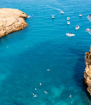 Aerial view of the famous cove in Polignano a Mare with turquoise water small boats and swimmers enjoying the sea surrounded by rocky cliffs in Polignano a Mare Apulia Italy. Aerial view of the famous cove in Polignano a Mare with turquoise water small boats and swimmers enjoying the sea surrounded by rocky cliffs in Polignano a Mare Apulia Italy.
