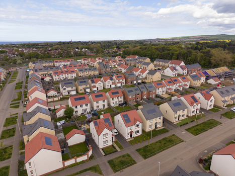 Aerial view of a modern residential neighborhood with solar panels on rooftops and lush green trees under a cloudy sky in Edinburgh Scotland United Kingdom.