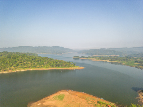 Aerial view of Wadaslintang Reservoir featuring lush green hills calm water and agricultural fields along the shoreline in Wadaslintang Central Java Indonesia. Aerial view of Wadaslintang Reservoir featuring lush green hills calm water and agricultural fields along the shoreline in Wadaslintang Central Java Indonesia.