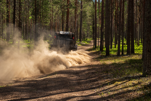 View of an off road vehicle driving through a pine forest and kicking up a large cloud of dust on a dirt track near Lake Ladoga in Sortavala Respublika Kareliya Russia.