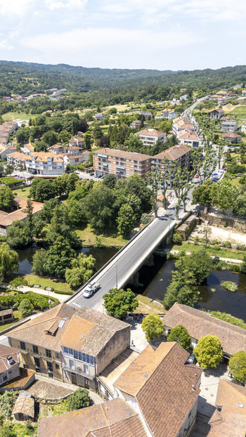 Aerial view of a bridge crossing a river surrounded by lush green trees and traditional stone buildings with terracotta roofs in Allariz Province of Ourense Spain. Aerial view of a bridge crossing a river surrounded by lush green trees and traditional stone buildings with terracotta roofs in Allariz Province of Ourense Spain.