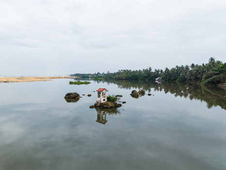 Aerial view of a small white shrine on a rocky outcrop in the middle of a calm river surrounded by lush palm trees under an overcast sky in Galle Southern Province Sri Lanka. Aerial view of a small white shrine on a rocky outcrop in the middle of a calm river surrounded by lush palm trees under an overcast sky in Galle Southern Province Sri Lanka.