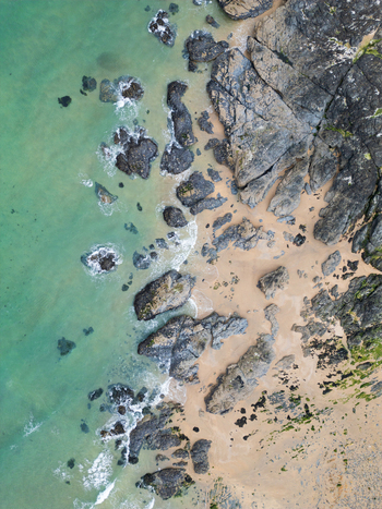 Aerial view of Godrevy Beach featuring turquoise ocean waves crashing against dark jagged rocks and golden sand in Gwithian England United Kingdom. Aerial view of Godrevy Beach featuring turquoise ocean waves crashing against dark jagged rocks and golden sand in Gwithian England United Kingdom.