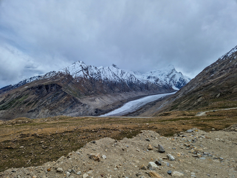 View of the Penzi La road winding through the rugged mountain landscape of Zanskar featuring snow capped peaks and a glacier under a cloudy sky in Zanskar Ladakh India.