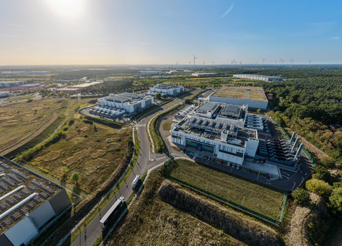 Aerial view of the Vantage Data Centers BER1 facility featuring modern industrial buildings surrounded by green fields and infrastructure in Ludwigsfelde Brandenburg Germany. Aerial view of the Vantage Data Centers BER1 facility featuring modern industrial buildings surrounded by green fields and infrastructure in Ludwigsfelde Brandenburg Germany.