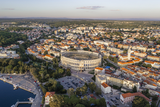 Aerial view of Pula Arena surrounded by historic stone buildings terracotta rooftops and lush greenery in the coastal city of Pula Istarska zupanija Croatia. Aerial view of Pula Arena surrounded by historic stone buildings terracotta rooftops and lush greenery in the coastal city of Pula Istarska zupanija Croatia.