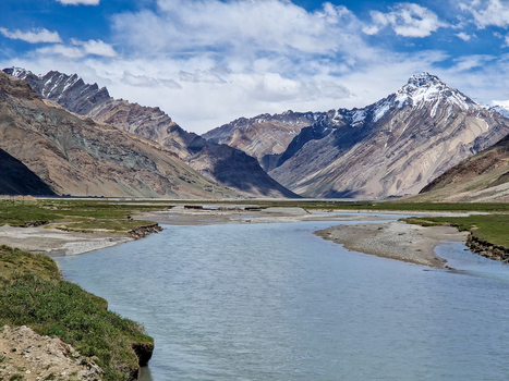 View of the Penzi La road winding through the dramatic Zanskar valley with snow capped Himalayan peaks a flowing river and lush green meadows in Zanskar Ladakh India.