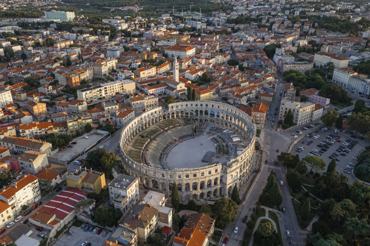 Aerial view of the ancient Roman Pula Arena amphitheater surrounded by the historic cityscape red tiled rooftops and urban streets in Pula Istarska zupanija Croatia. Aerial view of the ancient Roman Pula Arena amphitheater surrounded by the historic cityscape red tiled rooftops and urban streets in Pula Istarska zupanija Croatia.