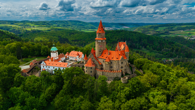 Aerial view of Bouzov Castle with its iconic red tiled roofs and tall central tower nestled among lush green forests under a dramatic cloudy sky Bouzov Olomoucky kraj Czechia. Aerial view of Bouzov Castle with its iconic red tiled roofs and tall central tower nestled among lush green forests under a dramatic cloudy sky Bouzov Olomoucky kraj Czechia.