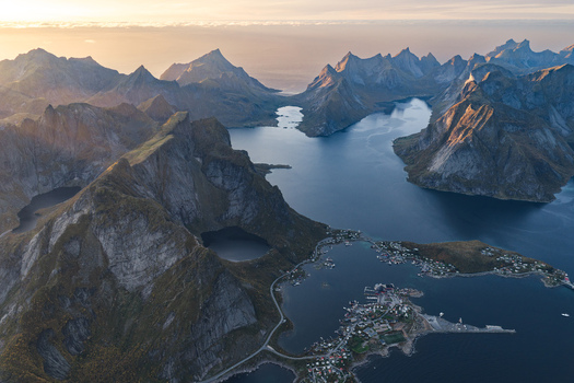 Aerial view of Lofoten islands featuring dramatic jagged mountain peaks deep blue fjords and a small coastal village with scattered houses in Leknes Nordland Norway. Aerial view of Lofoten islands featuring dramatic jagged mountain peaks deep blue fjords and a small coastal village with scattered houses in Leknes Nordland Norway.