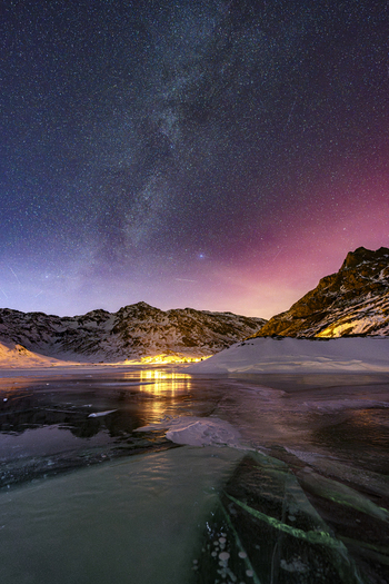 View of the Milky Way galaxy over a frozen lake and snow covered mountain peaks with a pink glow in the night sky Madesimo Lombardy Italy. View of the Milky Way galaxy over a frozen lake and snow covered mountain peaks with a pink glow in the night sky Madesimo Lombardy Italy.