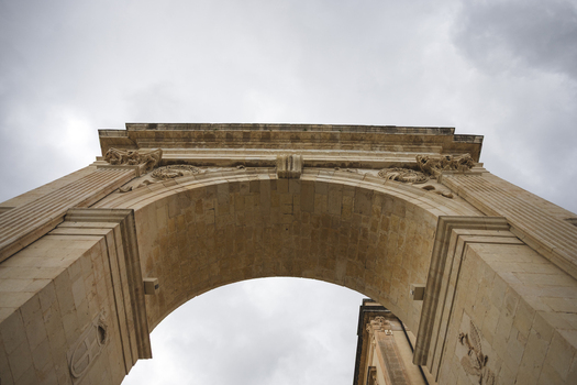 View of the historic Porta Reale triumphal arch with ornate stone carvings under a cloudy sky Noto Sicily Italy. View of the historic Porta Reale triumphal arch with ornate stone carvings under a cloudy sky Noto Sicily Italy.