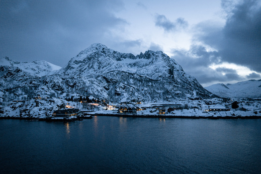Aerial view of snow laden mountains reflecting in the still waters lights twinkle along the shore Hamn Troms Norway. Aerial view of snow laden mountains reflecting in the still waters lights twinkle along the shore Hamn Troms Norway.