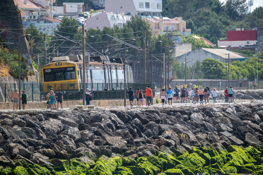 Cruz Quebrada Portugal 03 May 2026 View of a yellow CP train passing by the Passeio Maritimo de Alges with people walking along the waterfront path and rocky shoreline.