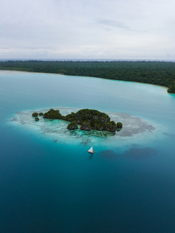 Aerial view of a solitary sailboat glides across the turquoise waters surrounding a verdant island a serene contrast to the distant dark forest Pine Island L Île des Pins New Caledonia. Aerial view of a solitary sailboat glides across the turquoise waters surrounding a verdant island a serene contrast to the distant dark forest Pine Island L Île des Pins New Caledonia.