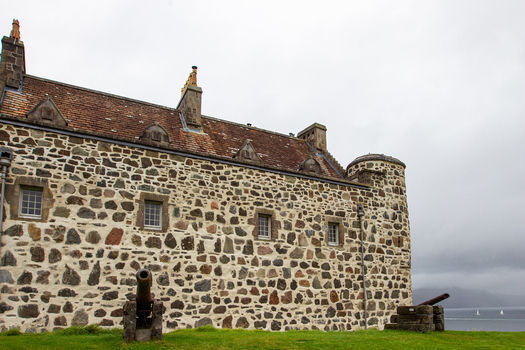 View of Duart Castle featuring historic stone walls and cannons on the grass overlooking the sea under a cloudy sky in Isle of Mull Scotland United Kingdom.