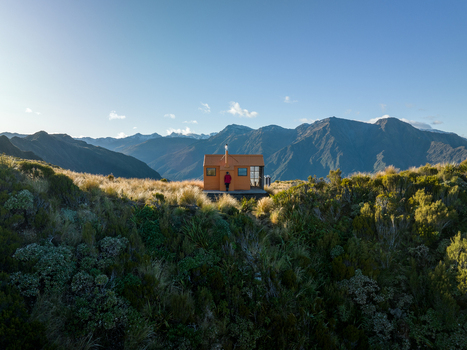 Aerial view of a solitary wooden cabin perched amidst the rugged grassy terrain nestled beneath distant towering mountain peaks Lake Kaniere West Coast Region New Zealand. Aerial view of a solitary wooden cabin perched amidst the rugged grassy terrain nestled beneath distant towering mountain peaks Lake Kaniere West Coast Region New Zealand.