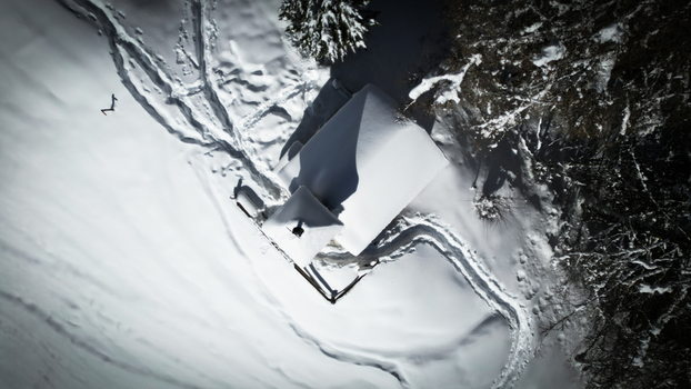 Aerial view of a snow covered building nestled among dark trees trails etched in the pristine white landscape Grimentz Valais Switzerland.