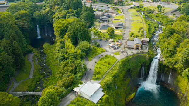 Aerial view of Shiraito Falls surrounded by lush green forest cascading water and rocky cliffs in Japan. Aerial view of Shiraito Falls surrounded by lush green forest cascading water and rocky cliffs in Japan.