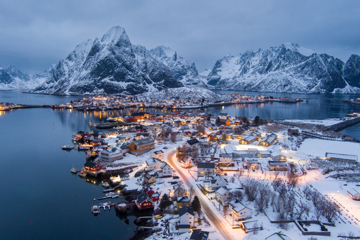 Aerial view of Lofoten village with snow covered houses illuminated streets and dramatic mountains in Nordland Norway.