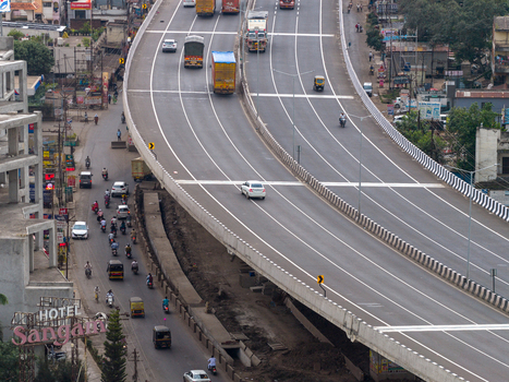 Aerial view of a busy highway flyover with vehicles traveling along the road adjacent to local streets with traffic and buildings in Karad Maharashtra India.