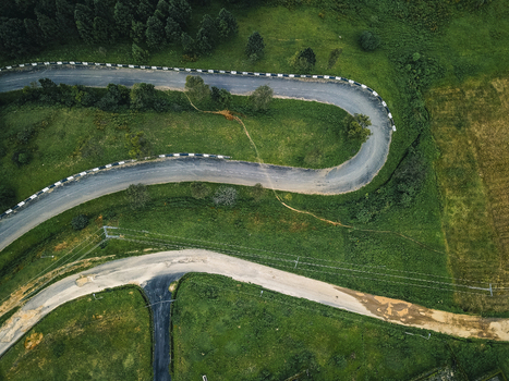 Aerial view of a winding asphalt road with white and black barriers carving through vibrant green hills and dark forest Obudu Cross River Nigeria.