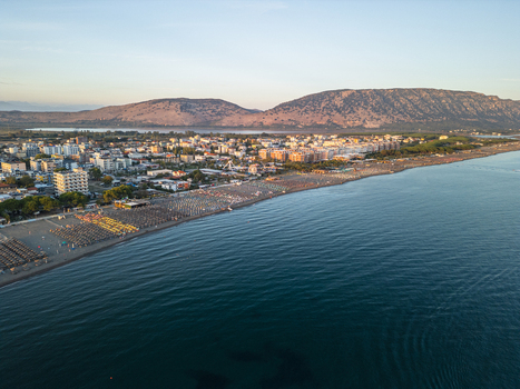 Aerial view of Velipoja Beach with rows of colorful umbrellas on the sandy shore coastal town buildings and mountains in the background in Velipoje Shkoder County Albania.