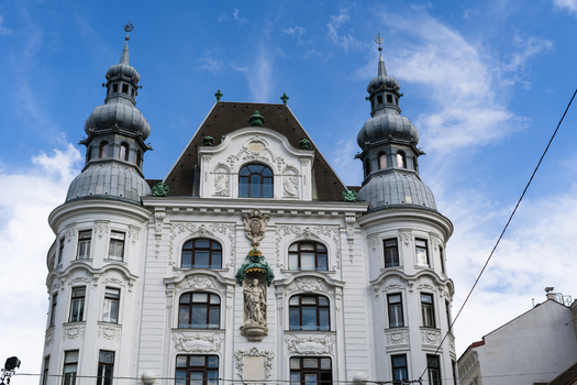 View of an ornate historic building facade with twin grey domes and a central statue under a blue sky in Vienna Vienna Austria. View of an ornate historic building facade with twin grey domes and a central statue under a blue sky in Vienna Vienna Austria.