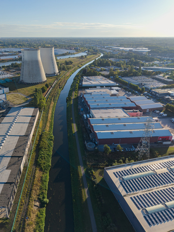 Aerial view of industrial infrastructure featuring large cooling towers a canal and warehouses with solar panels in Vilvoorde Flanders Belgium.