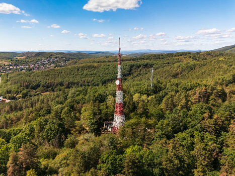 Aerial view of a red and white telecommunications tower rising above forested hills near Salgotarjan Hungary with a rural settlement and distant mountains. Aerial view of a red and white telecommunications tower rising above forested hills near Salgotarjan Hungary with a rural settlement and distant mountains.