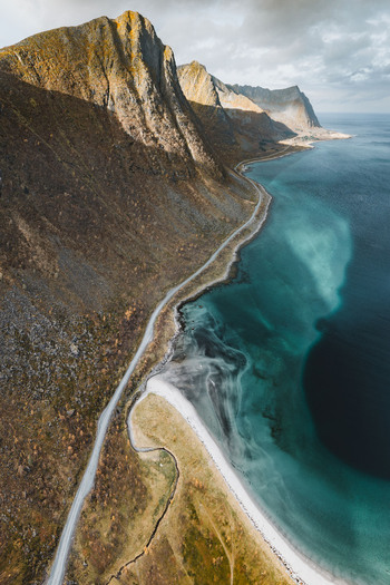 Aerial view of the dramatic coastal landscape of Senja with steep mountains a winding road along the turquoise shoreline and rocky terrain in Senja Troms Norway.