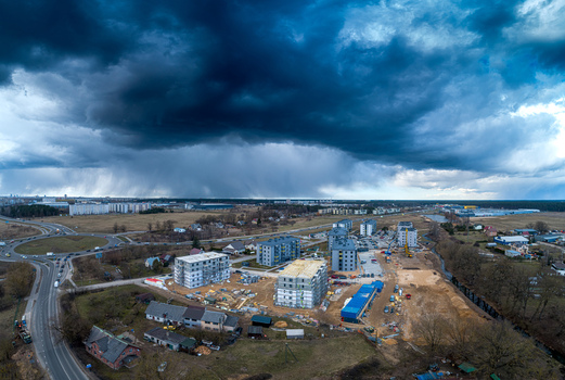 Aerial view of a construction site featuring new apartment buildings a nearby roundabout and surrounding rural landscape under a dramatic dark stormy sky in Latvia. Aerial view of a construction site featuring new apartment buildings a nearby roundabout and surrounding rural landscape under a dramatic dark stormy sky in Latvia.