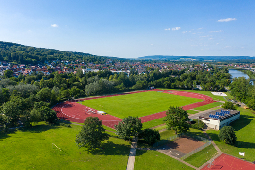 Aerial view of Sport Island Forchheim featuring a red running track and green athletic field surrounded by lush trees and the town skyline in Forchheim Bavaria Germany. Aerial view of Sport Island Forchheim featuring a red running track and green athletic field surrounded by lush trees and the town skyline in Forchheim Bavaria Germany.