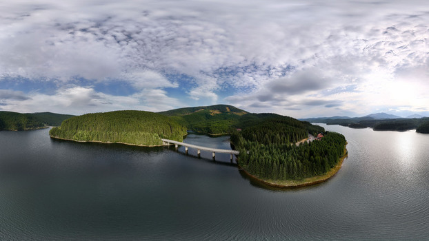 Aerial view of a bridge crossing a large lake surrounded by dense pine forests and rolling hills in Transylvania Romania.