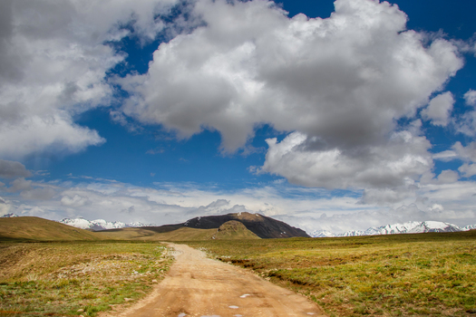 View of a dirt road winding through the high altitude plateau of Deosai National Park with snow capped mountains under a cloudy sky Skardu Gilgit Pakistan. View of a dirt road winding through the high altitude plateau of Deosai National Park with snow capped mountains under a cloudy sky Skardu Gilgit Pakistan.