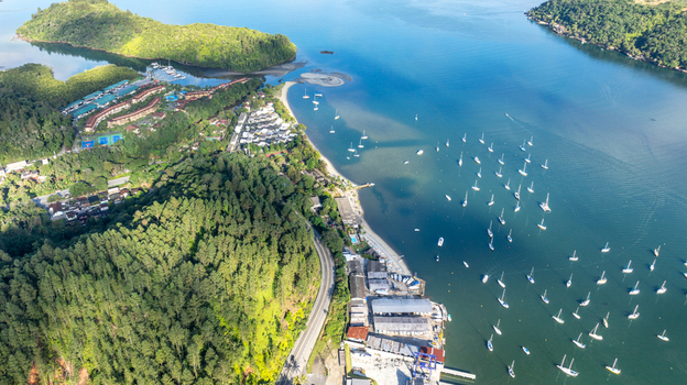 Aerial view of a coastal bay with numerous sailboats lush green hills a winding road and residential buildings along the shoreline in Angra dos Reis State of Rio de Janeiro Brazil.