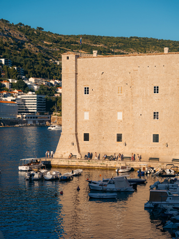 View of St. John s Fortress with people walking along the pier and small boats moored in the harbor in Dubrovnik Dubrovnik Neretva County Croatia. View of St. John s Fortress with people walking along the pier and small boats moored in the harbor in Dubrovnik Dubrovnik Neretva County Croatia.