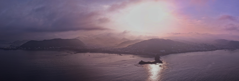 Aerial view of a coastal landscape featuring rolling hills a small peninsula extending into the calm sea and a vibrant purple sky during the golden hour Japan.
