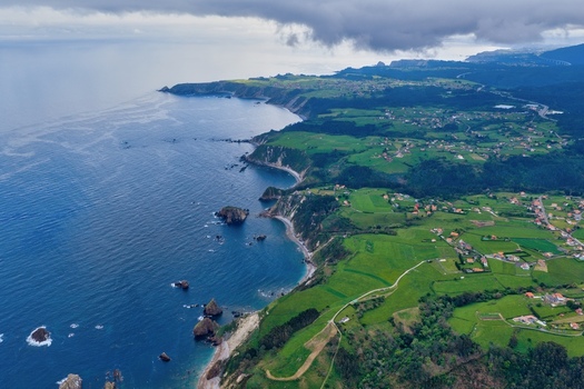 Aerial view of Silence Beach Viewpoint and the rugged coastline with lush green fields and steep cliffs along the Cantabrian Sea in Cudillero Asturias Spain.