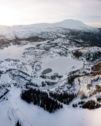 Aerial view of Gaustablikk Fjellresort nestled in the snowy mountains of Rjukan featuring ski slopes frozen lakes and pine forests under soft winter light. Rjukan Telemark Norway. Aerial view of Gaustablikk Fjellresort nestled in the snowy mountains of Rjukan featuring ski slopes frozen lakes and pine forests under soft winter light. Rjukan Telemark Norway.